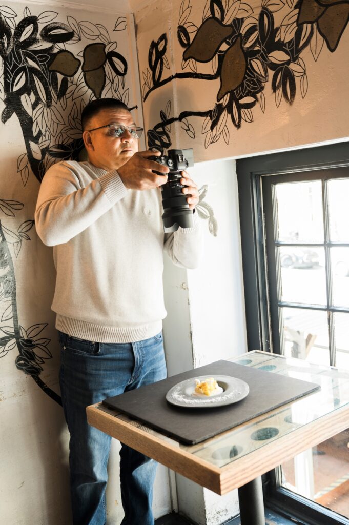 Behind the scenes of Savor The Light food photography workshop in San Francisco, showing a participant capturing a styled food scene in natural light at Bouche SF.