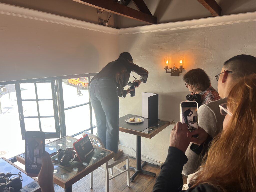 Behind-the-scenes moment of Cyntia Apps adjusting light and composition during a live food shoot demonstration at her photography workshop.