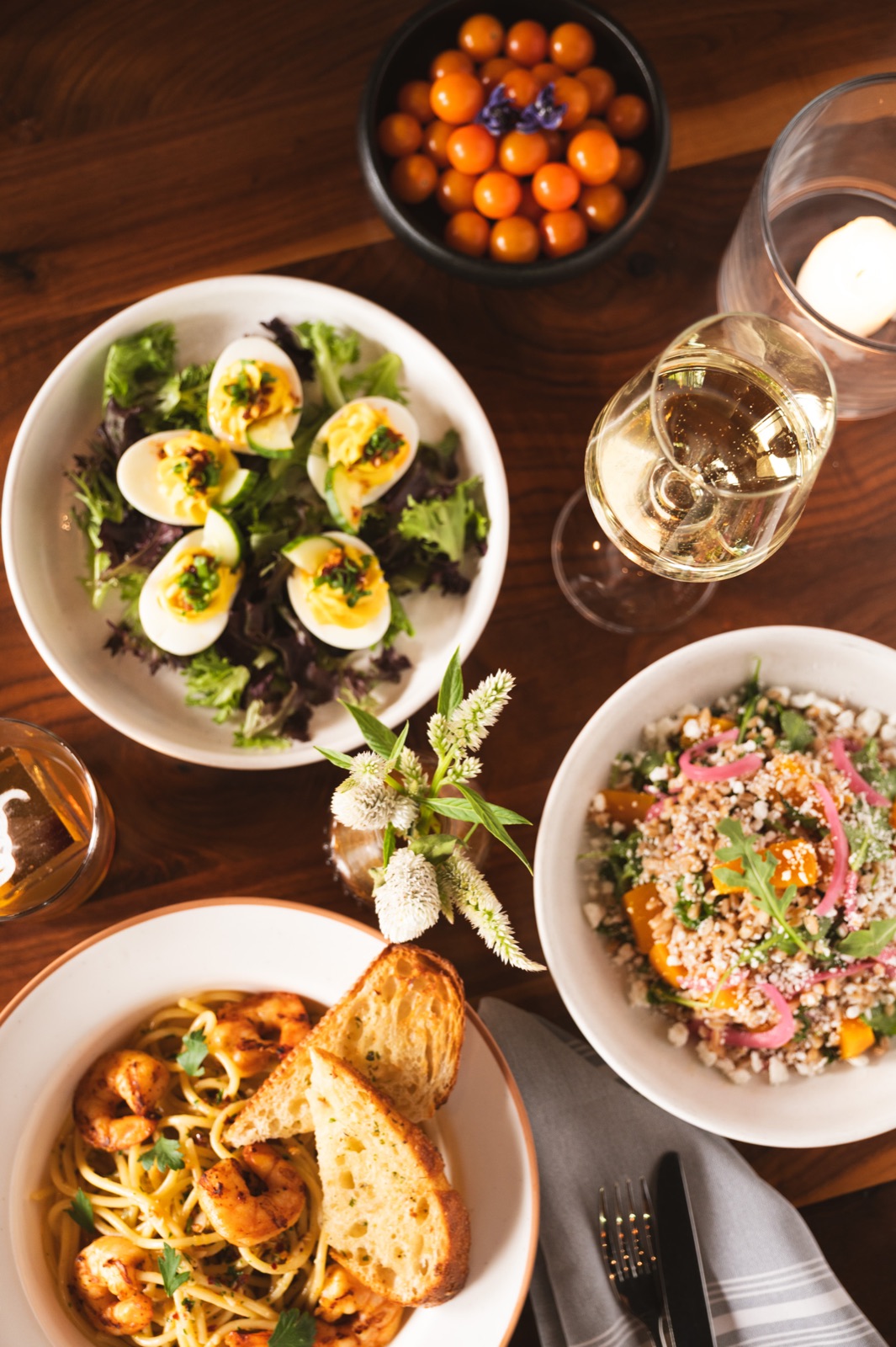 Overhead arrangement of pasta, deviled eggs, salad, and drinks on a wooden table.