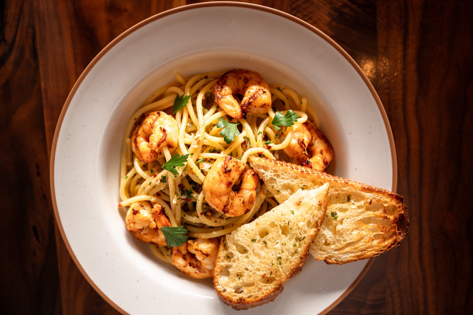 Overhead view of pasta and toasted bread on a wooden table.